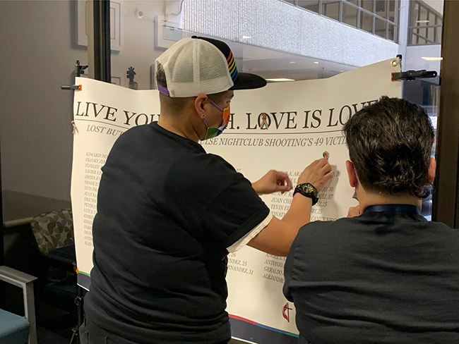 Men and women adding rainbow pins to Live Your Truth Love is Love banner