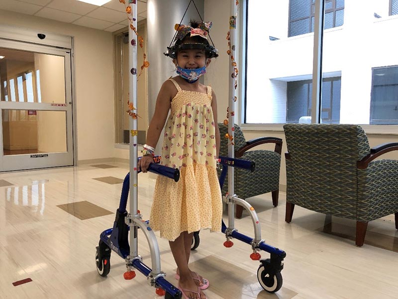 Little girl wearing yellow dress practicing walking in hospital with metal walker device