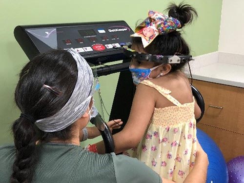 Medical professional talking to little girl during while on treadmill in hospital rehabilitation gym