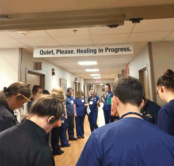a group of staff praying in a hospital hallway