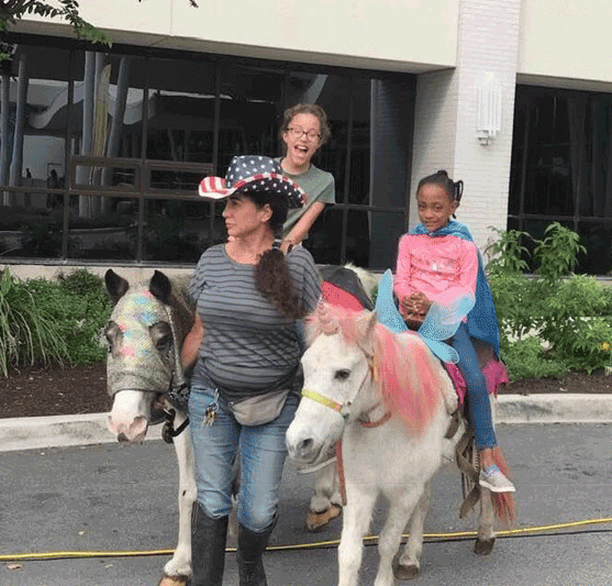hospital staff riding ponies with dyed manes, dressed up with a small child