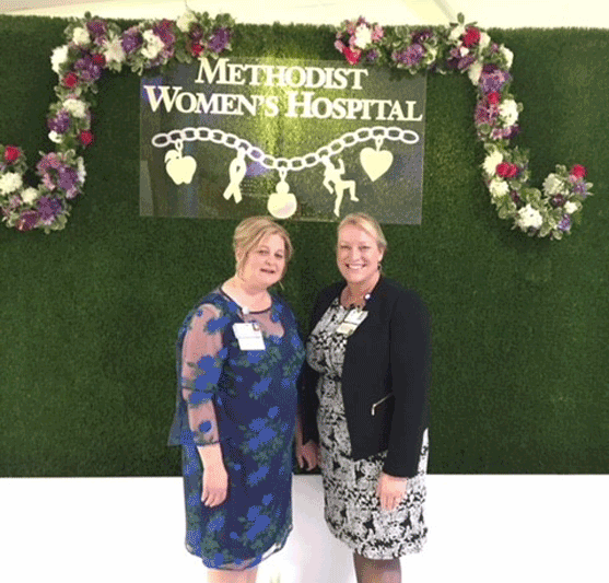 2 women in dresses standing below a sign crested with flowers that reads 'methodist women's hospital'